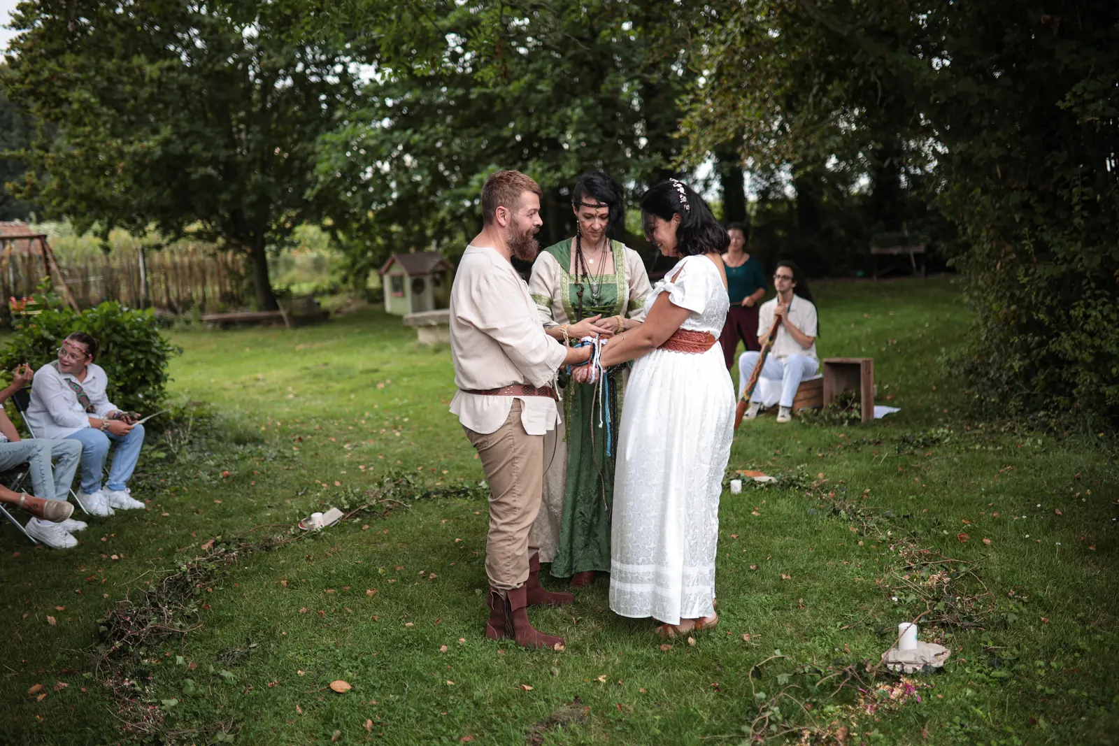 Les mariés et l'officiante au centre du cercle tracé dans l'herbe d'un jardin